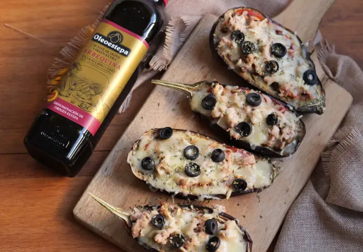 Berenjenas rellenas gratinadas con queso y aceitunas negras, junto a una botella de aceite de oliva virgen extra Oleoestepa.