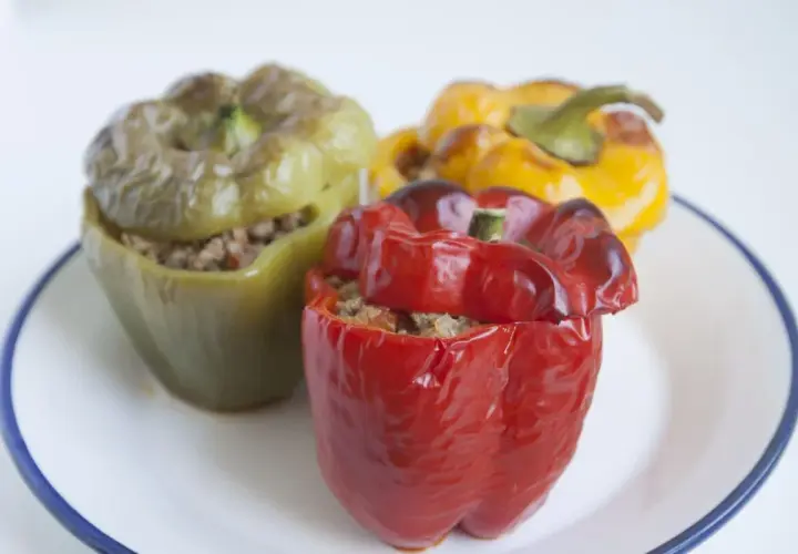 Tres pimientos rellenos, uno rojo, uno verde y uno amarillo, servidos en un plato blanco con borde azul.