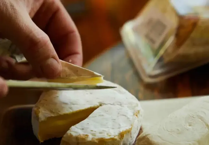 Mano cortando un queso de Tetilla con un cuchillo. Se ve la corteza blanca y el interior cremoso.