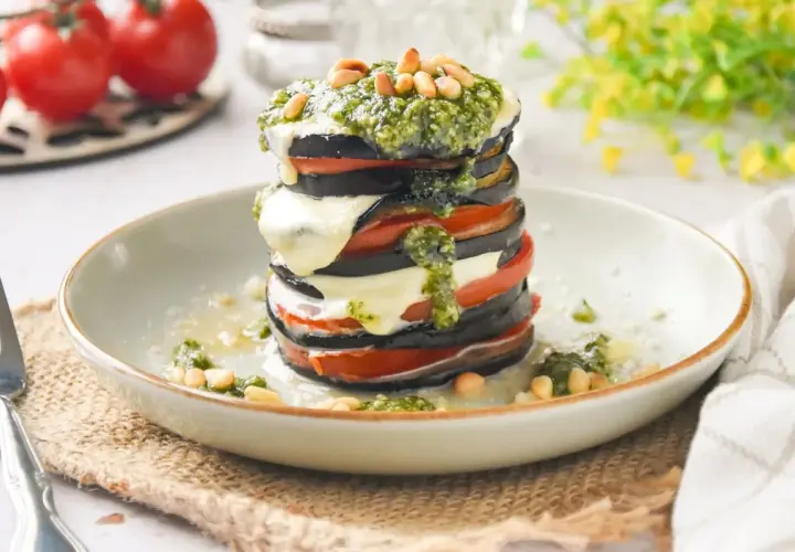 Deliciosa milhoja de berenjena con tomate, mozzarella fundida y pesto, coronada con piñones. Un plato ligero y sabroso.