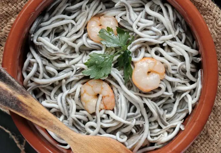 Deliciosas recetas con gulas y gambas, servidas en cazuela de barro con perejil y cuchara de madera.