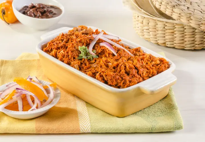 Cochinita pibil, un platillo yucateco de cerdo deshebrado en achiote, servido con cebolla morada y naranja.
