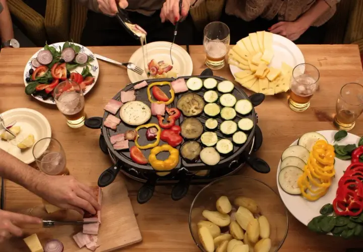Mesa con raclette, queso, verduras y patatas. ¡Ideas raclette para una cena divertida!