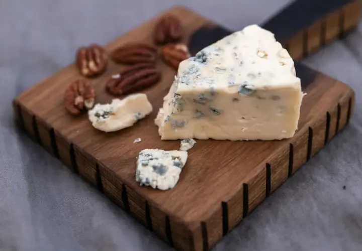 Un trozo de queso azul, ideal para la flora intestinal, reposa sobre una tabla de madera junto a nueces pecanas.