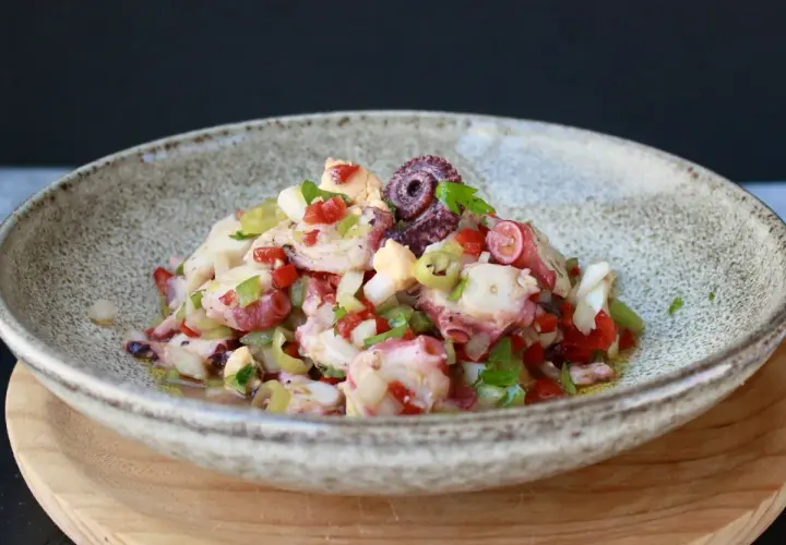 Un refrescante salpicón de pulpo con pimientos, cebolla y aceitunas, servido en un cuenco rústico.