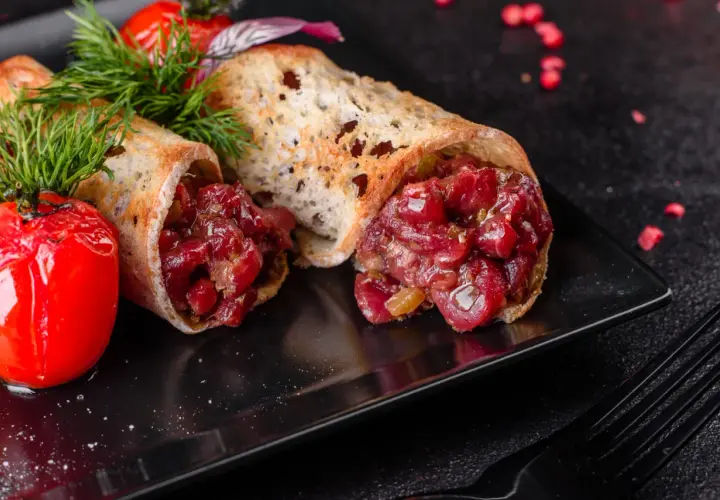 Delicioso steak tartar servido en pan tostado, acompañado de tomates cherry asados y eneldo fresco.