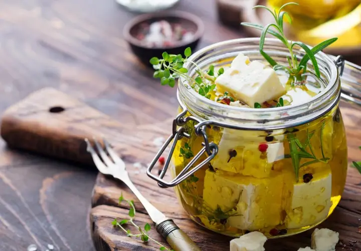Queso en aceite de oliva, con hierbas aromáticas y granos de pimienta, listo para disfrutar.