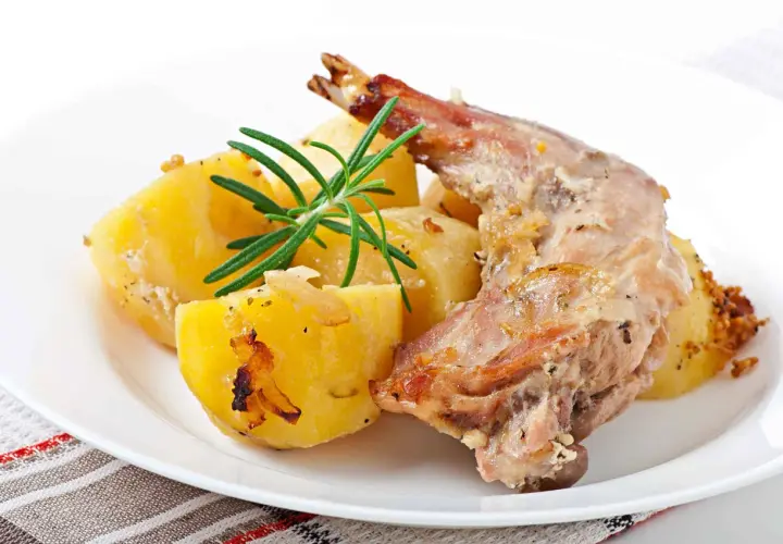 Conejo al horno jugoso con patatas asadas y romero fresco. Un plato tradicional y delicioso.