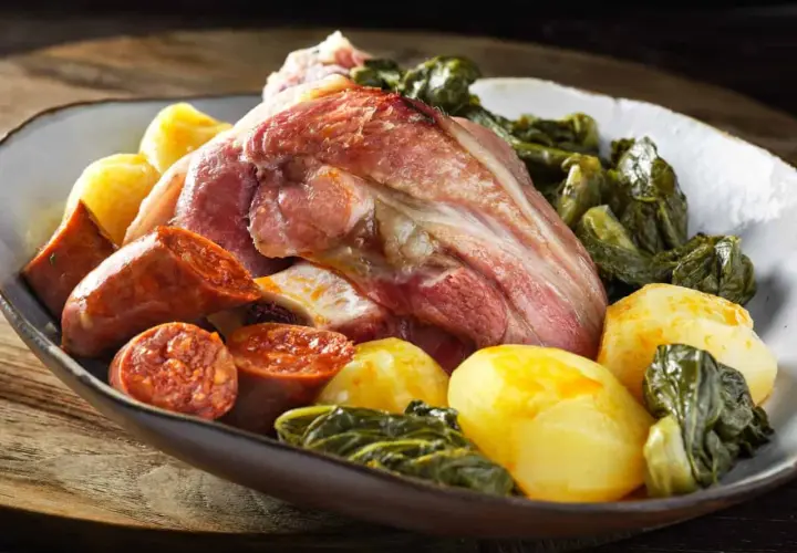 Un plato generoso de lacon con grelos, acompañado de chorizo y patatas cocidas, listo para ser disfrutado.