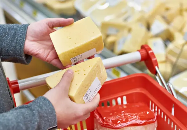 Manos sostienen trozos de queso cheddar, buscando opciones sin lactosa en el supermercado.