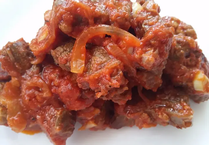 Un plato humeante de carne con tomate y cebolla, cocinado a fuego lento hasta que la carne esté tierna y la salsa espesa.