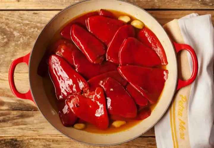 Pimientos del piquillo asados en una cazuela roja, con ajos y un paño de cocina.