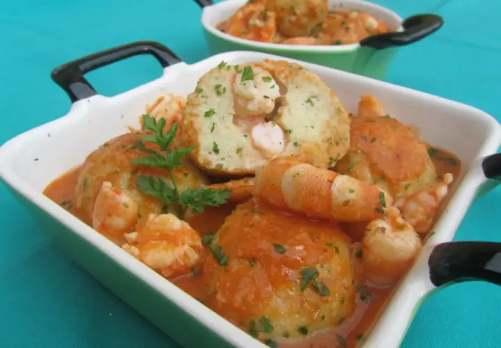 Deliciosas albóndigas de rape con gambas en salsa de tomate, adornadas con perejil fresco.