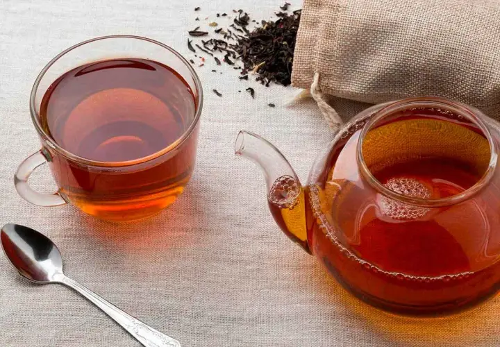 Una taza y tetera de té negro, con hojas secas esparcidas. ¿A que sabe el té negro? A un sabor robusto y reconfortante.