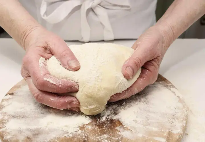 Manos amasando masa con harina, preparando diferentes tipos de levadura para panadería.