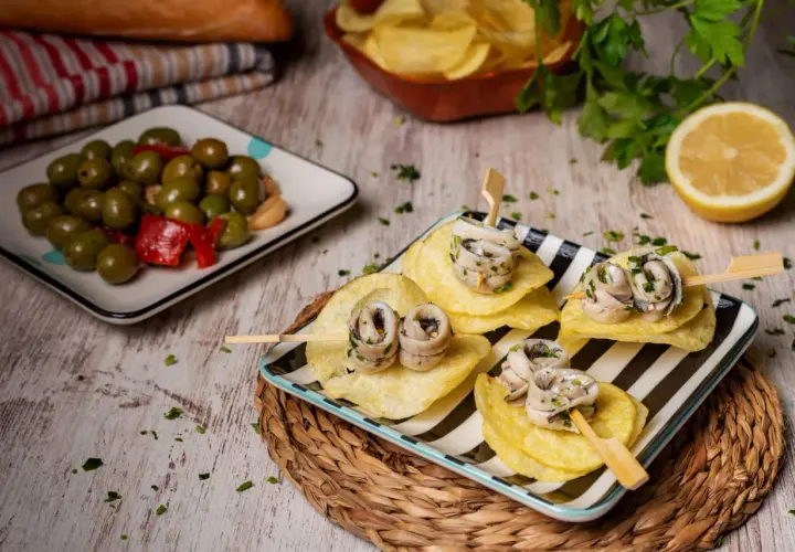 Deliciosas recetas con anchoas: pinchos de anchoas enrolladas sobre patatas fritas, acompañadas de aceitunas y limón.