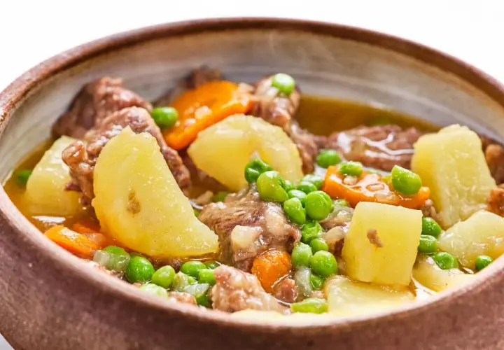 Un reconfortante ragú de ternera con patatas, zanahorias y guisantes en un cuenco de barro.