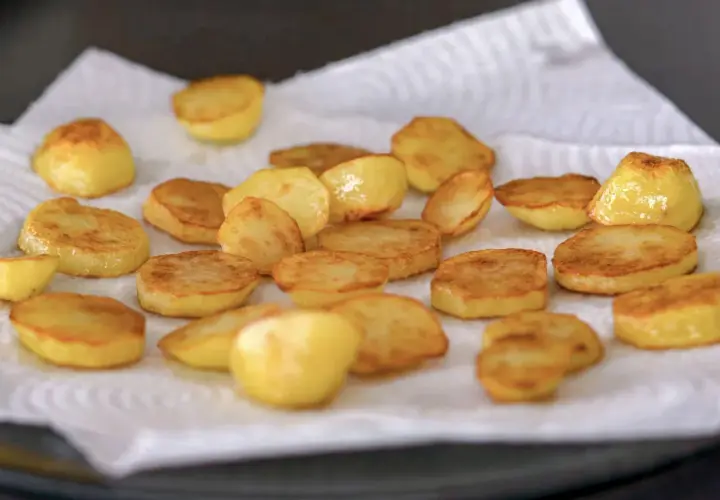Rodajas doradas de patatas al horno, recién salidas de la sartén y escurriendo el exceso de aceite sobre papel de cocina.
