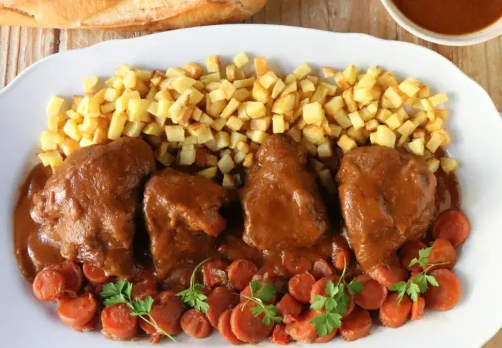 Delicioso jarrete de ternera estofado en salsa, acompañado de patatas fritas y zanahorias.