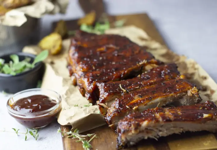 Costillas de cerdo al horno, jugosas y glaseadas, servidas con salsa barbacoa y hierbas frescas. ¡Un festín irresistible!