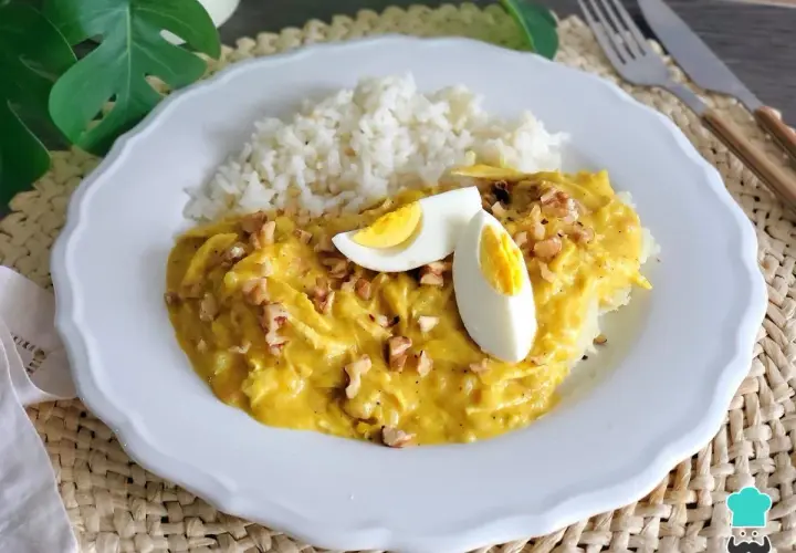 Un plato de aji de pollo cremoso con arroz blanco, huevo duro y nueces picadas.