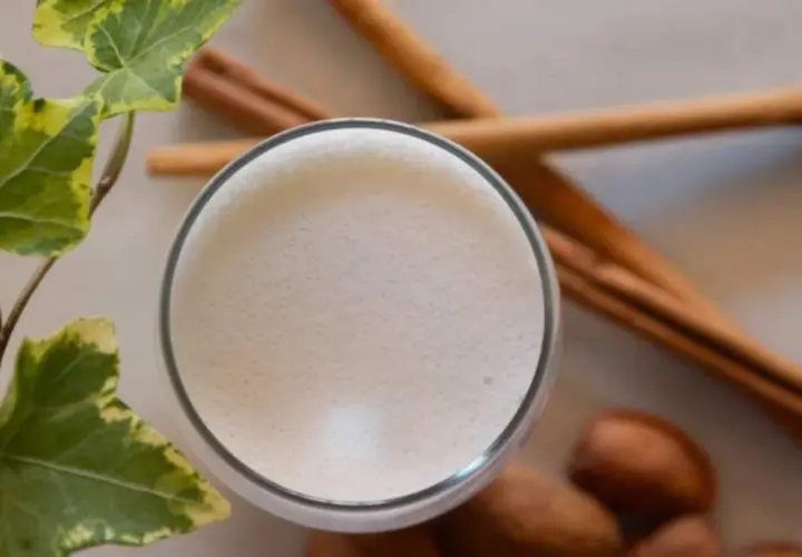 Un vaso de leche espumosa, canela y hojas verdes, recordatorio de los beneficios de la leche de vaca para una vida saludable.