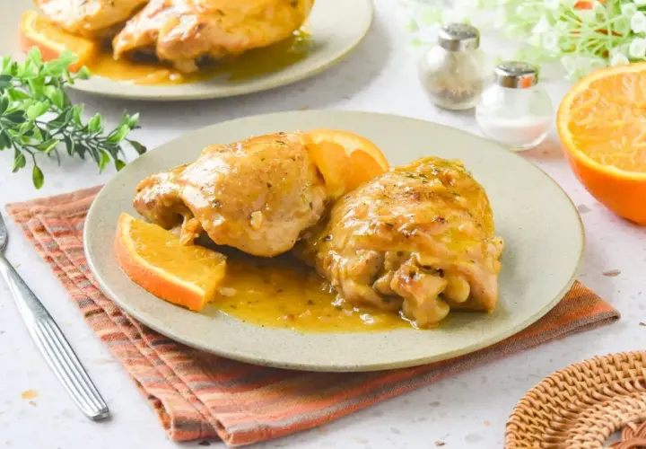 Dos jugosas piezas de pollo a la naranja, bañadas en su salsa y decoradas con gajos de naranja fresca. Un plato delicioso y aromático.