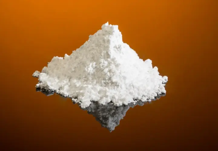 Montículo de polvo blanco fino, que es el cremor tártaro, sobre una superficie reflectante naranja.