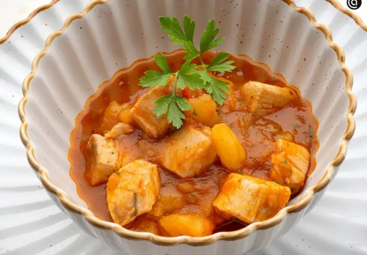 Un delicioso marmitako de bonito con patatas y pimientos en una cazuela, adornado con perejil fresco.