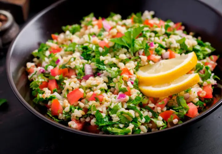 Delicioso tabule receta, una ensalada fresca de bulgur, tomate, perejil y cebolla morada, adornada con rodajas de limón.