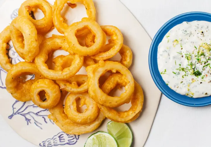Crujientes aros de cebolla dorados, servidos con una cremosa salsa y gajos de lima. ¡Un aperitivo irresistible!