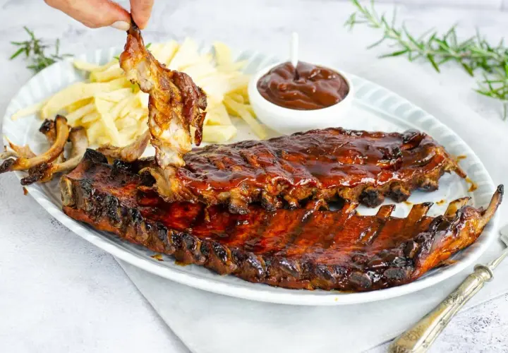 Costillas a la barbacoa jugosas y glaseadas, servidas con patatas fritas y salsa barbacoa. ¡Un festín para los sentidos!