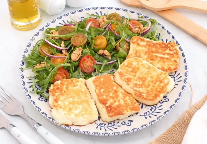 Ensalada fresca con tomates cherry, cebolla morada y nueces, acompañada de trozos dorados de ser halloumi a la plancha.