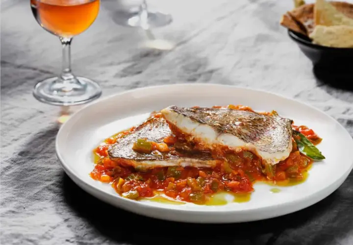 Deliciosa urta a la roteña servida en plato blanco, con guarnición de pimientos y tomate. Acompañada de copa de vino y pan.