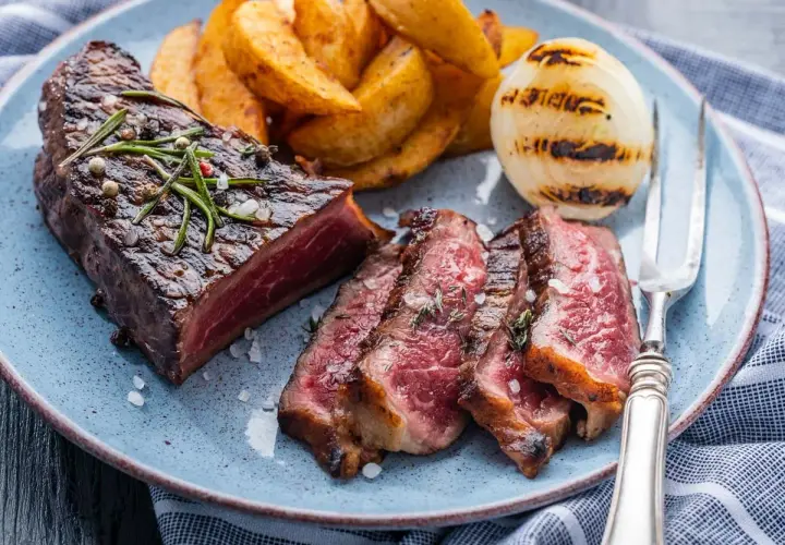 Jugoso entrecot a la plancha, cortado en rodajas, acompañado de patatas gajo y cebolla a la parrilla.