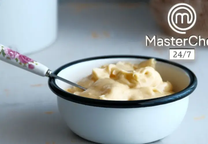 Crema sedosa lista para emulsionar en cocina. Un tazón blanco con borde negro contiene una suave crema amarilla, con una cuchara de mango floral.