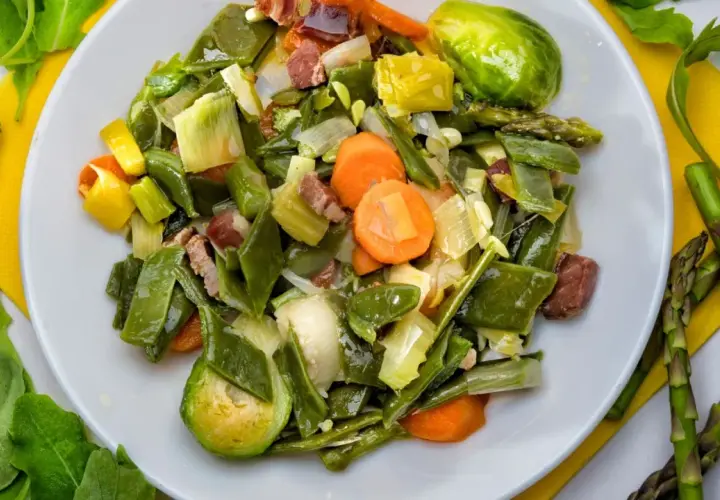 Un plato de menestra de verduras con judías verdes, zanahorias, puerros y trozos de jamón.