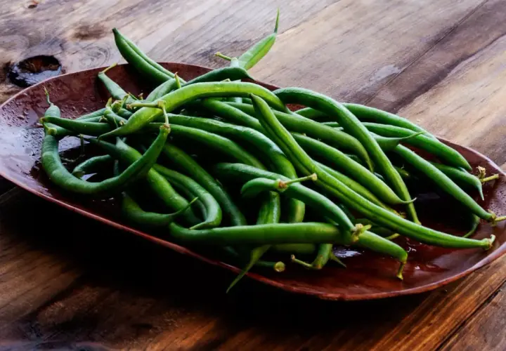 Un plato de judías verdes frescas y vibrantes sobre una mesa de madera rústica, listas para ser cocinadas.