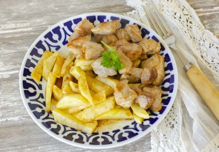 Raxo con patatas, un plato tradicional gallego, servido en un plato azul y blanco con perejil fresco.