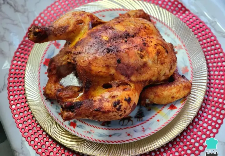 Un jugoso pollo a la brasa, dorado y crujiente, servido en un plato festivo con motivos navideños.