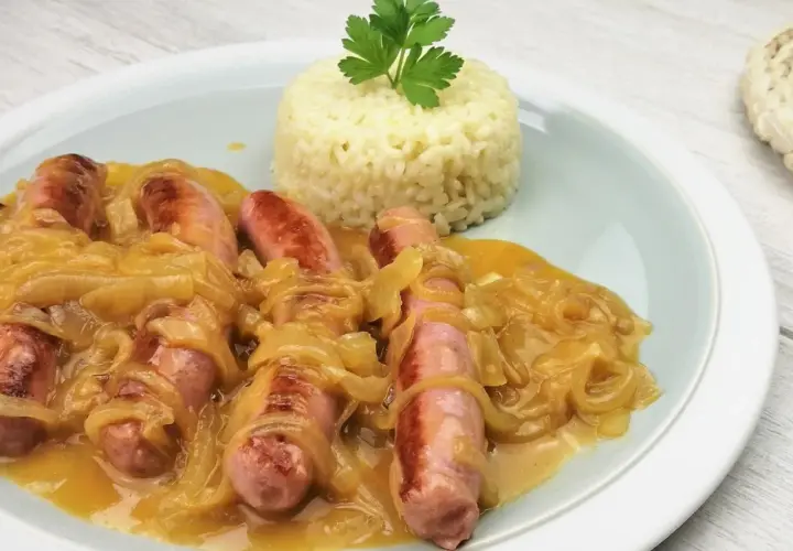 Salchichas al vino con cebolla caramelizada y una porción de arroz blanco, decorado con perejil.