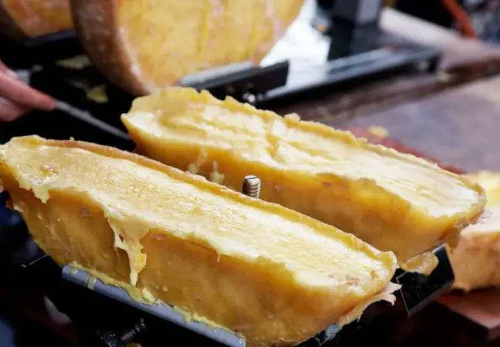 Dos mitades de queso fundido en una máquina para raclette, con el queso derritiéndose y goteando.