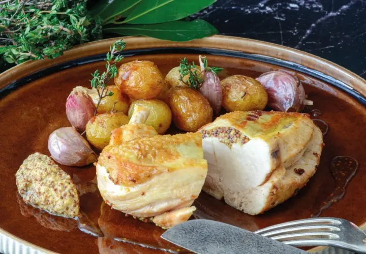 Pollo asado con patatas y ajos, acompañado de una generosa porción de mostaza de grano entero, mostrando varios tipos de mostaza.