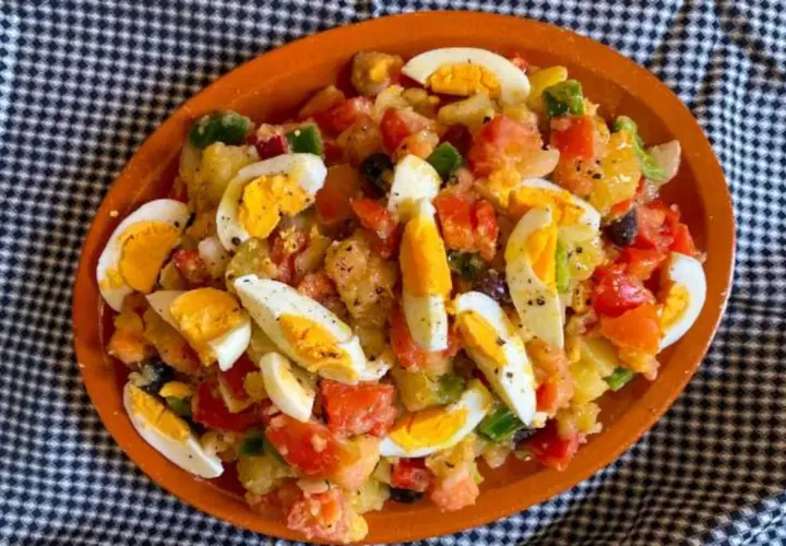 Ensalada campera con patatas, tomate, pimiento, aceitunas y huevos duros, servida en plato de barro.