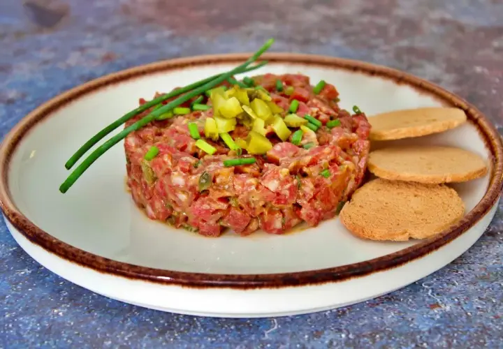 Tartar de salchichón finamente picado, adornado con pepinillos y cebollino, servido con tostas.