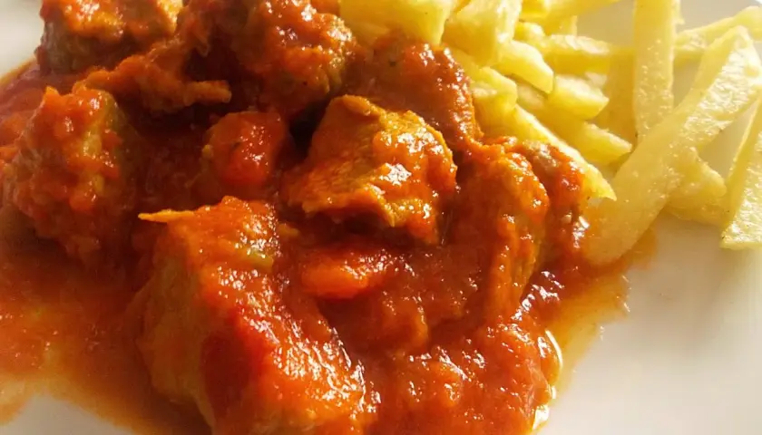 Magro con tomate, jugoso y tierno, servido con patatas fritas crujientes. Un plato casero que reconforta el alma.