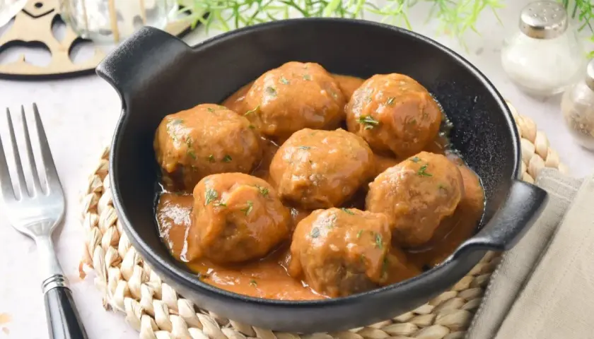 Deliciosas albóndigas caseras en salsa, perfectas para tu próxima receta. Servidas en un cuenco negro con un tenedor al lado.