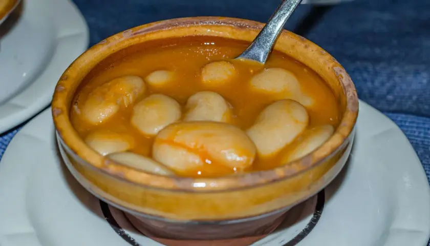 Un cuenco de barro rebosante de judiones de la granja en una salsa dorada, con una cuchara lista para servir.