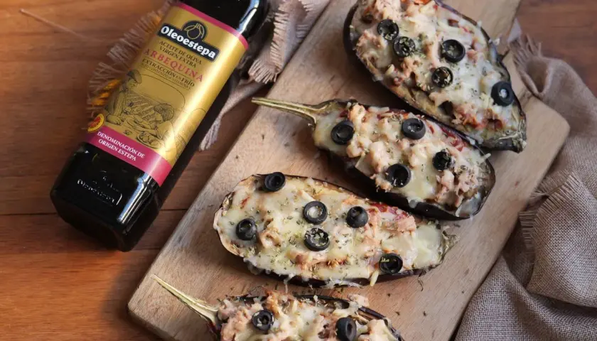 Berenjenas rellenas gratinadas con queso y aceitunas negras, junto a una botella de aceite de oliva virgen extra Oleoestepa.
