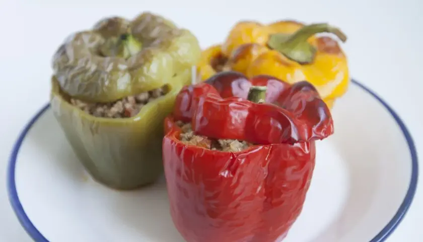 Tres pimientos rellenos, uno rojo, uno verde y uno amarillo, servidos en un plato blanco con borde azul.